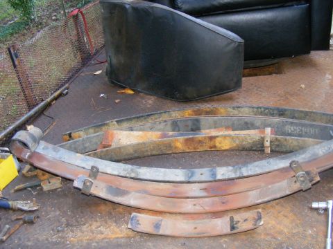 1978 Ford Bronco - Several rusty leaf springs are laid out on a trailer, with a black seat visible behind them.