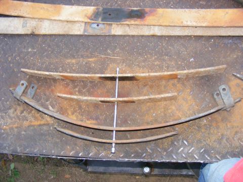 1978 Ford Bronco - Several leaf springs are arranged on a metal surface, with a central bolt holding them together.