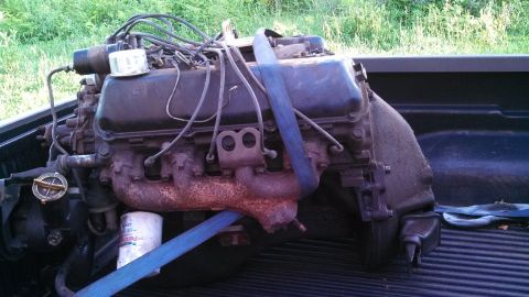 1979 Ford Bronco - Engine is secured with a blue strap in the bed of a pickup truck.