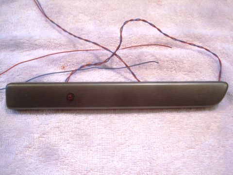 1993 Ford Bronco - This dark gray interior trim piece features a small red lens and exposed wires, likely a component from a vehicle's interior.
