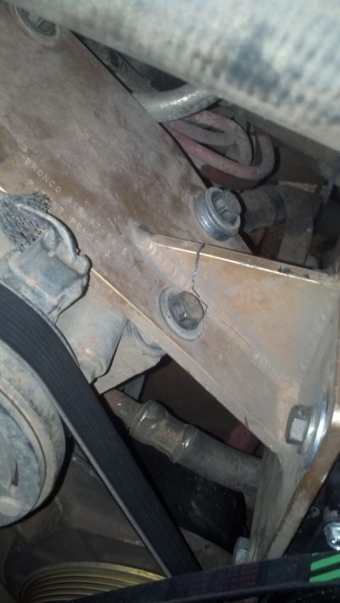 1990 Ford Bronco - Close-up of a damaged engine bracket with visible bolts and a drive belt.