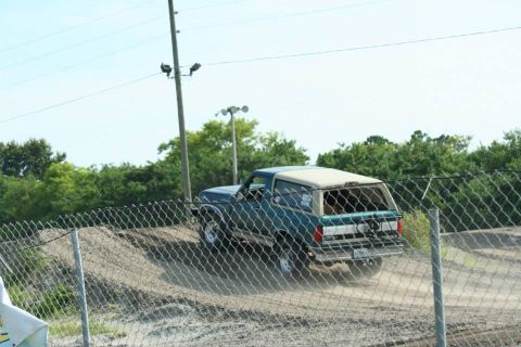 1996 Ford Bronco - A two-tone Ford Bronco navigates a dirt course, kicking up dust.