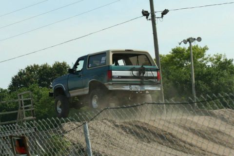 1996 Ford Bronco - A Ford Bronco navigates a dirt track, kicking up dust as it ascends a hill.