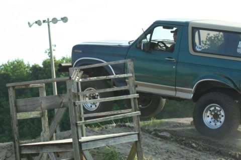 1996 Ford Bronco - 1996 Ford Bronco navigates an off-road course with a wooden structure in the foreground.
