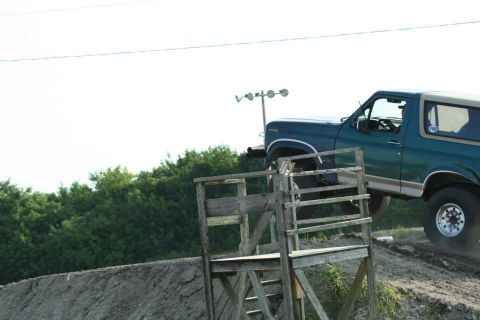 1996 Ford Bronco - A Ford Bronco is positioned on a dirt ramp, with a wooden structure nearby.