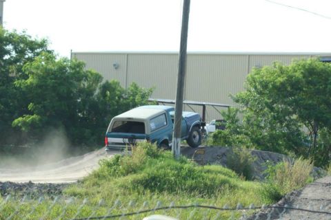 1996 Ford Bronco - Teal 1996 Ford Bronco with a white roof drives on a dirt road near a building.