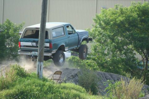 1996 Ford Bronco - This lifted Ford Bronco is airborne, clearing a dirt obstacle with dust trailing behind.