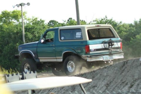 1996 Ford Bronco - This Ford Bronco is kicking up dust as it climbs a dirt incline, with a spare tire carrier mounted on its rear.