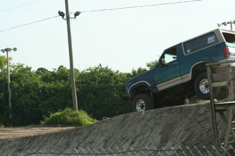1996 Ford Bronco - A Ford Bronco navigates a dirt ramp, its right front tire lifted high.