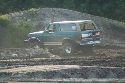 1996 Ford Bronco - This SUV is navigating a muddy off-road course, kicking up dirt as it goes.
