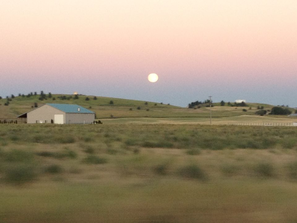 Moon hangs in a pink sky over a barn and rolling hills