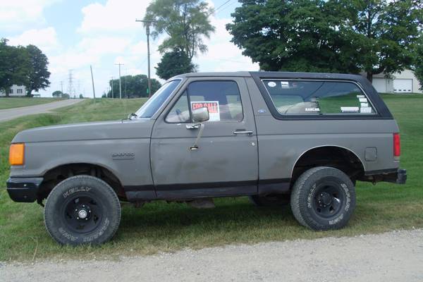 1987 Ford Bronco parked on grass with a 'For Sale' sign in the window