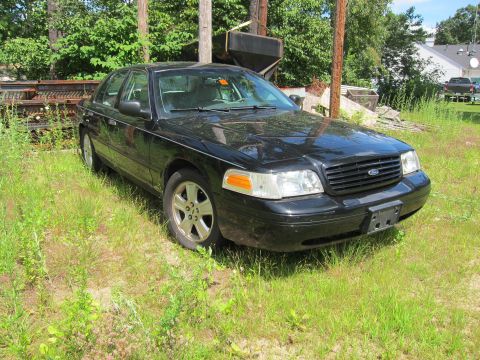 2001 Ford Crown Victoria - A black 2001 Ford Crown Victoria sits in a grassy area with trees and debris in the background.