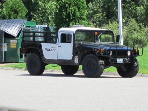 2001 Ford Crown Victoria - This Humvee police truck is parked on a paved surface with trees and dumpsters in the background.
