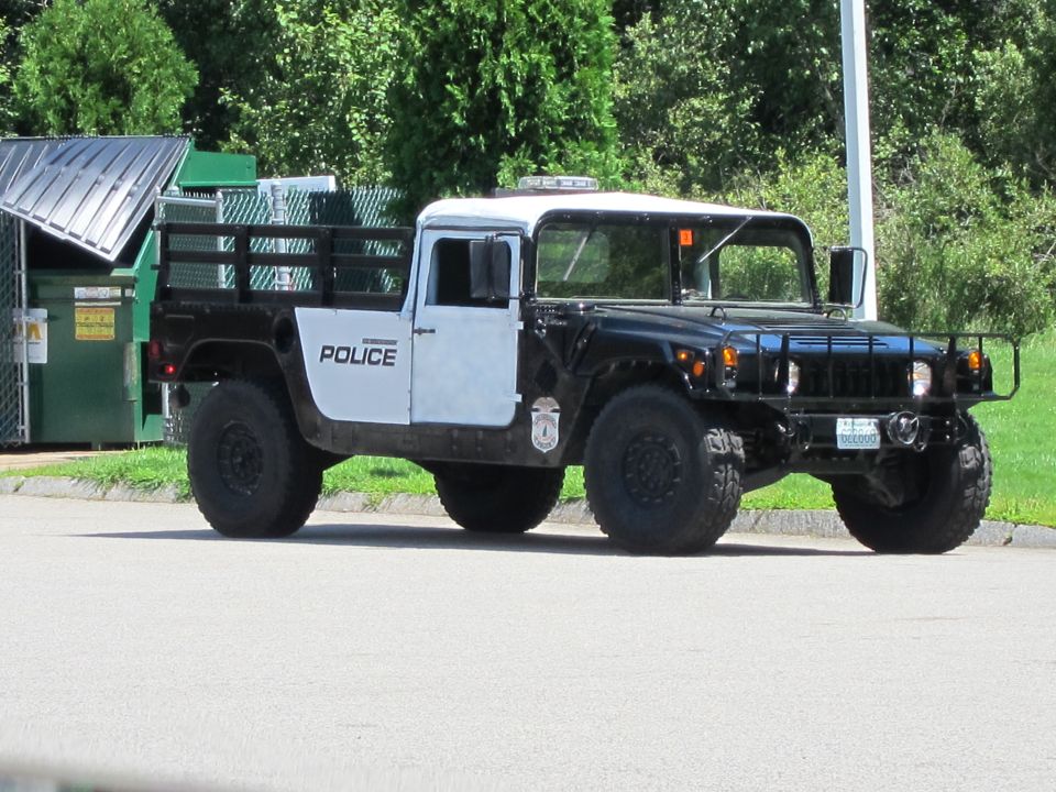 Police Humvee truck with black body and white doors, parked near dumpsters