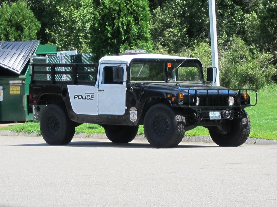 Black and white Humvee police truck with "POLICE" on the door, parked on asphalt