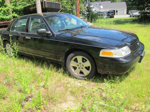 2001 Ford Crown Victoria - A black 2001 Ford Crown Victoria sits in a grassy area, with a utility trailer and houses in the background.