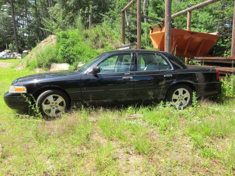 2001 Ford Crown Victoria - A black 2001 Ford Crown Victoria sedan is parked in a grassy area with some industrial equipment in the background.