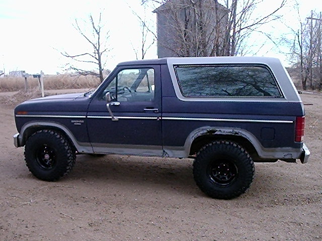Side view of a 1985 Ford Bronco with large tires and a silver top