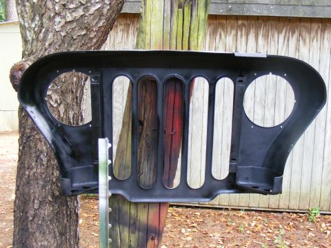1978 Ford Bronco - A black Jeep grille is displayed outdoors, mounted on wooden posts against a wooden fence.