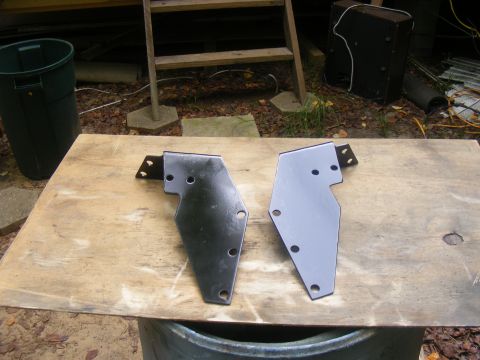 1978 Ford Bronco - Two metal brackets are laid out on a wooden surface, with a green trash can and wooden stairs in the background.