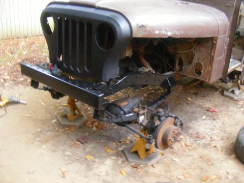 1978 Ford Bronco - A Jeep CJ-5 front clip is disassembled and supported by jack stands, showing its rusty hood and new bumper.