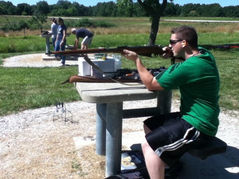 2006 Ford E350 - A man takes aim with a rifle at an outdoor shooting range, with other people visible in the background.