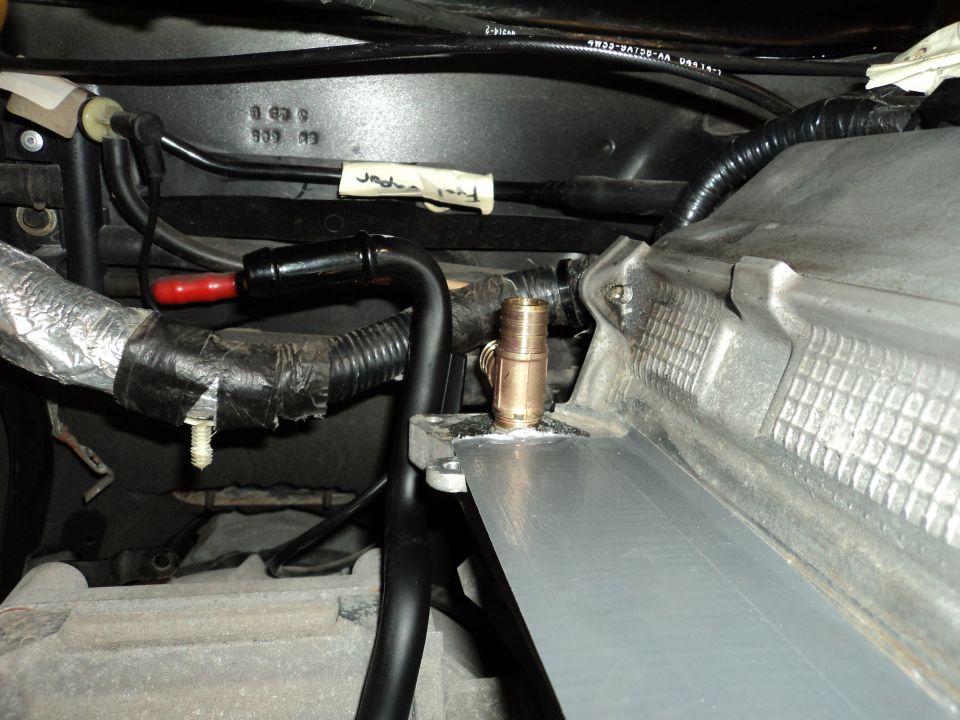Close-up of engine bay hoses and fittings, with some tape and a white label