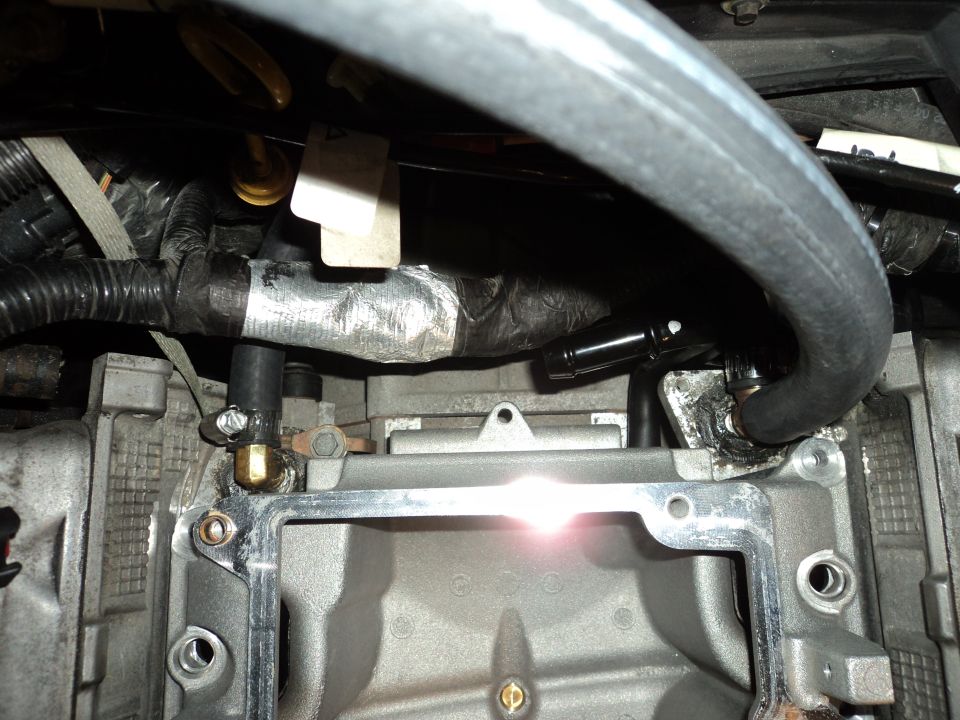 Close-up of engine components with hoses and wiring. Shows part of the intake manifold