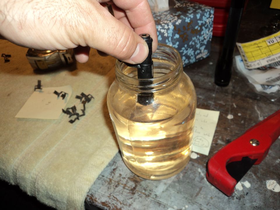 Hand holding a black part in a jar of clear liquid, with SuperMotors logo