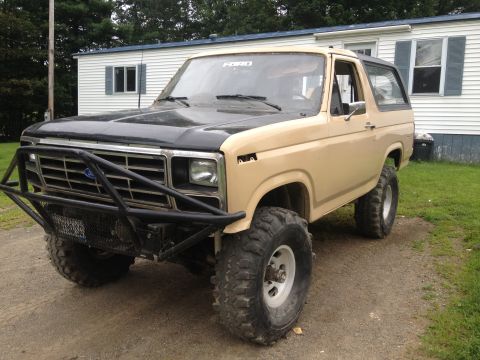 Tan 1978 Ford Bronco with black hood and off-road bumper, parked on dirt