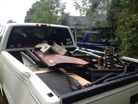 White pickup truck bed loaded with scrap metal and car parts, blue pickup truck in background