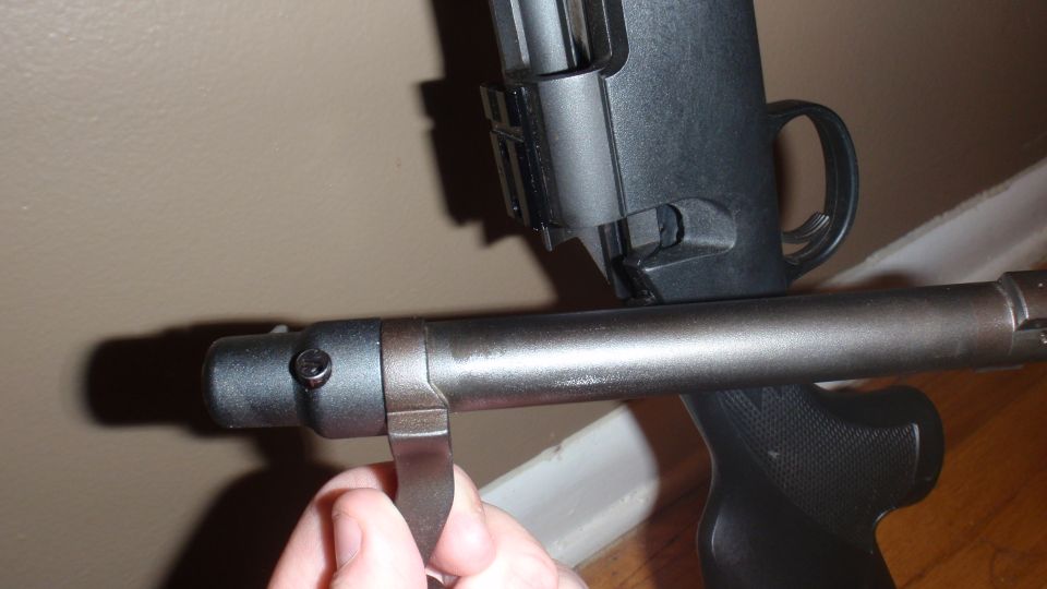 Close-up of a firearm barrel and receiver assembly, with a hand holding a metal piece near the muzzle