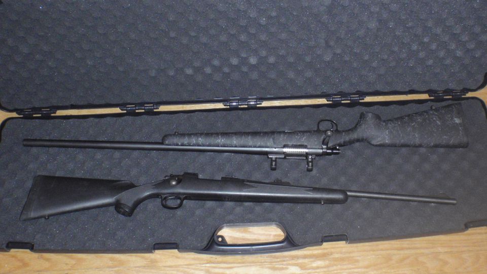 Two rifles, one with a camouflage stock and a long barrel, the other black with a shorter barrel, lie in a black foam-lined case