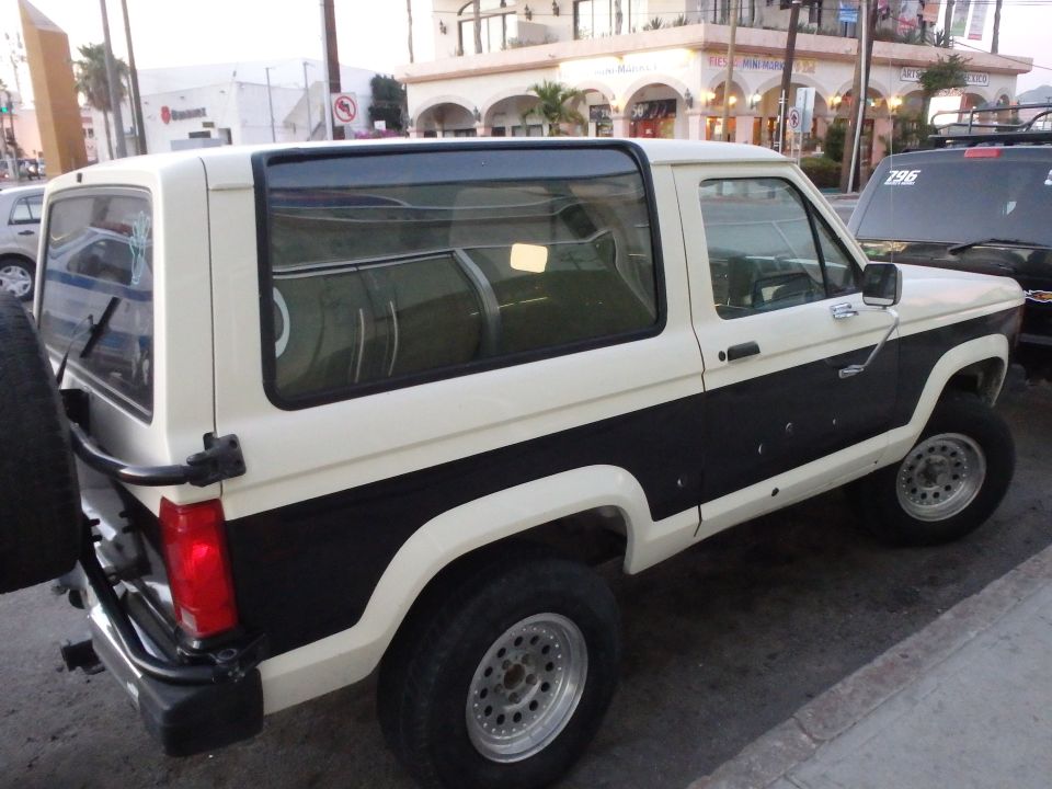 White and black Ford Bronco II with a spare tire mounted on the rear, parked on a street