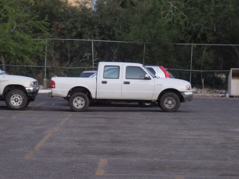 Side view of a white 2000 Ford Ranger SuperCab pickup truck parked next to another truck