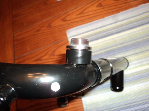 2004 Mercury Grand Marquis - A polished black tubular part photographed on a hardwood floor and striped cloth, with a machined aluminum plug or bung capped into a boss…