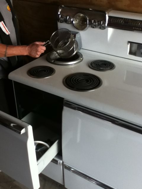2006 Ford E350 - A person is using a metal basket on a vintage white electric stove with four burners.