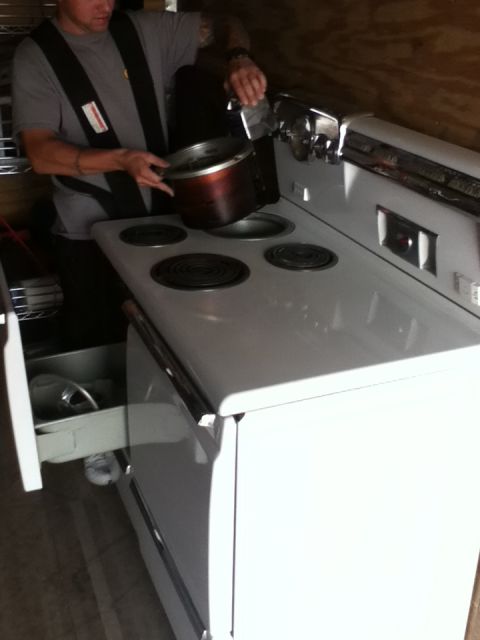 2006 Ford E350 - A person is placing a pot on a white electric stove, with a drawer pulled out below.