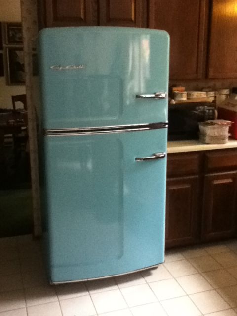 2006 Ford E350 - An aqua-colored retro refrigerator with chrome accents stands in a kitchen next to wooden cabinets.