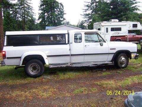 1988 Suzuki Samurai - A white Dodge Ram pickup truck with a camper shell is parked outside on a cloudy day.