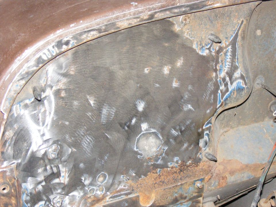 Close-up of a rusty metal panel showing weld repairs and grinding marks