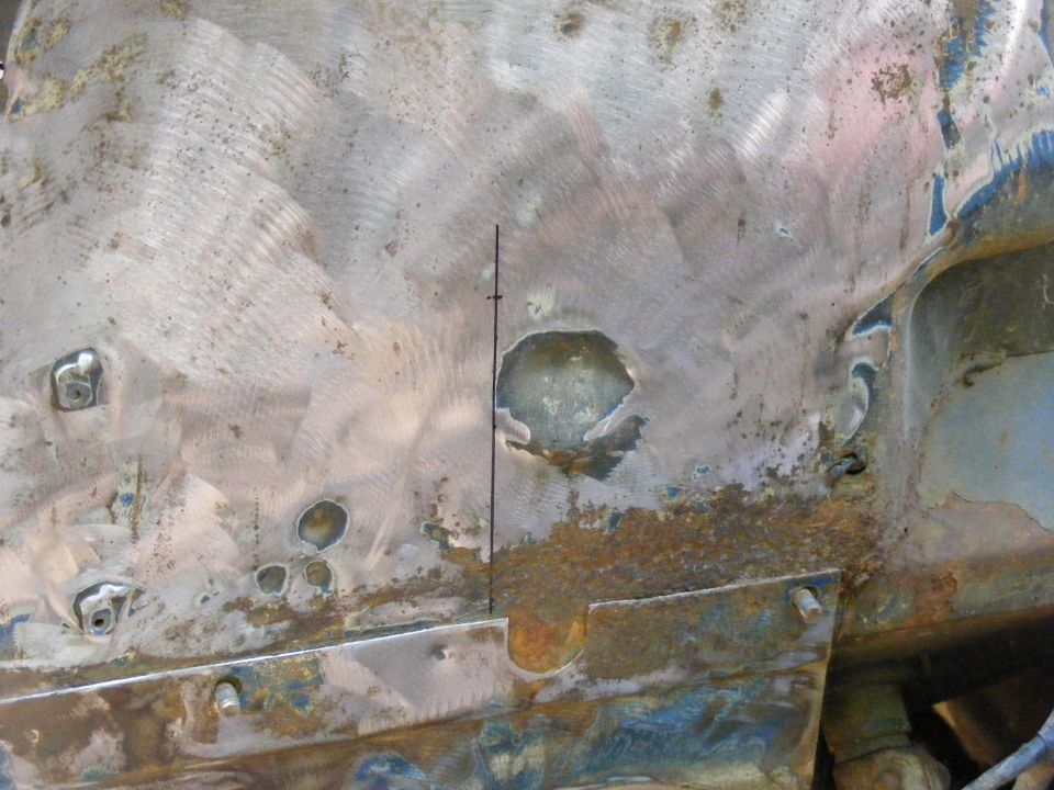 Close-up of rusted and damaged vehicle frame with holes and metal repairs