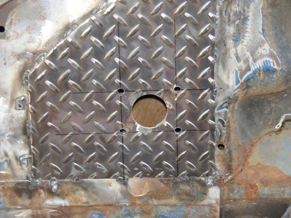 Diamond plate metal patch welded onto rusty vehicle floor, with a central hole and four smaller holes drilled around it