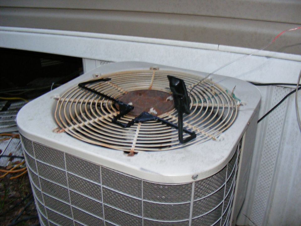 Top view of an outdoor air conditioning unit fan with a rusted center and protective cage