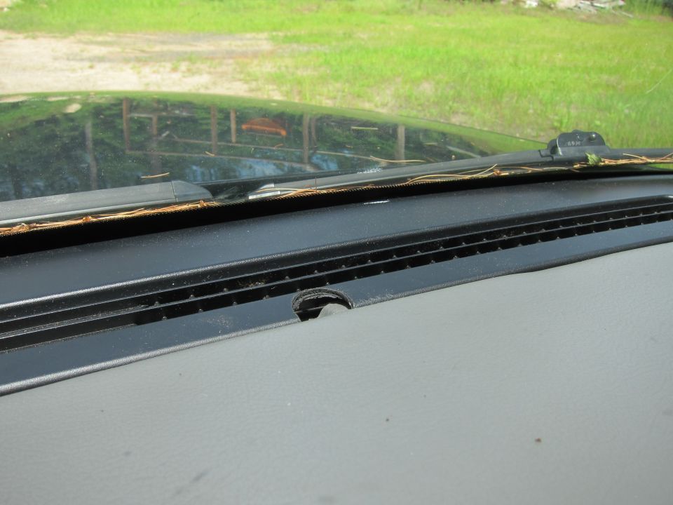 Dashboard and windshield area of a car, with grass and a fence reflected in the windshield
