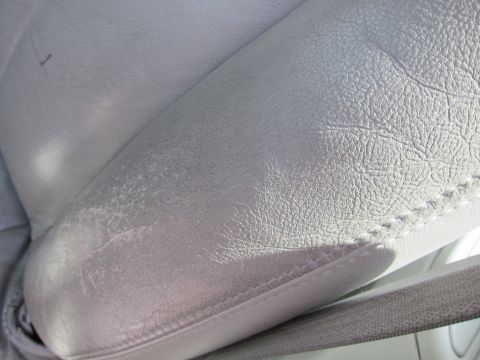2001 Ford Crown Victoria - The interior of a vehicle shows a close-up view of a light gray leather seat with signs of wear and visible stitching.
