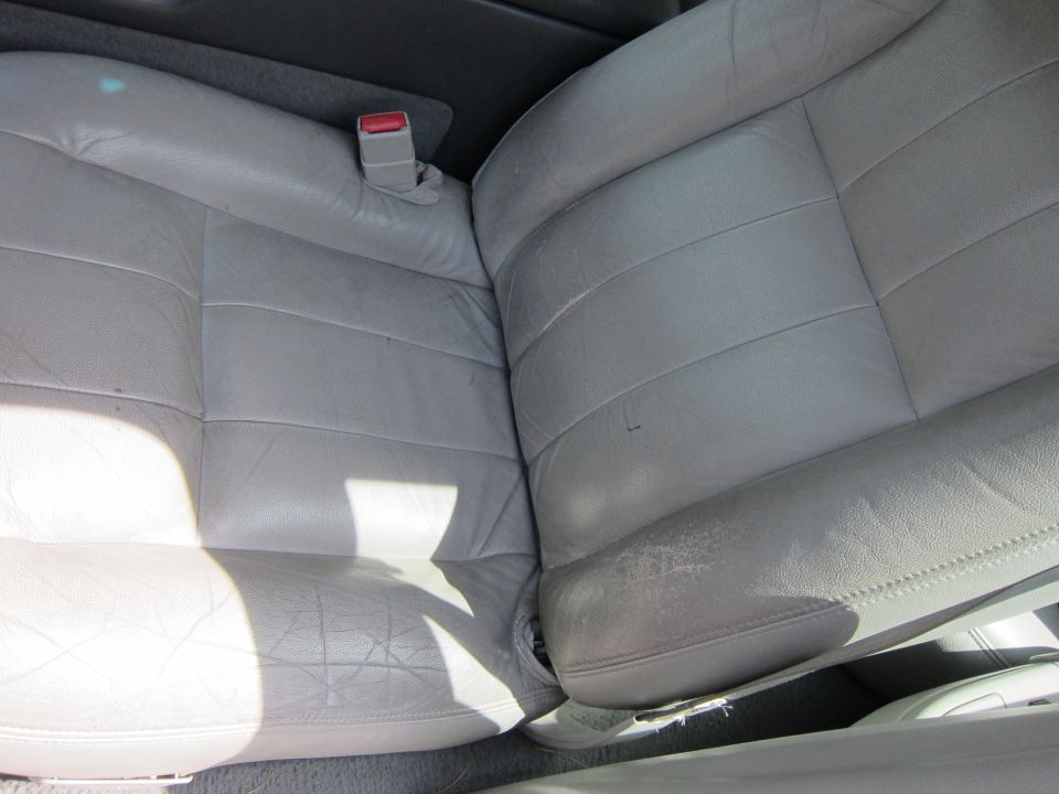Close-up of worn light gray leather car seats with visible creasing and some peeling on the right seat bolster