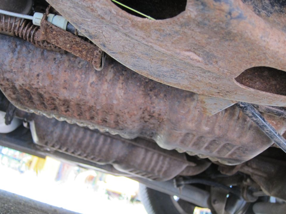 Underside of a vehicle showing rusty exhaust components and suspension parts