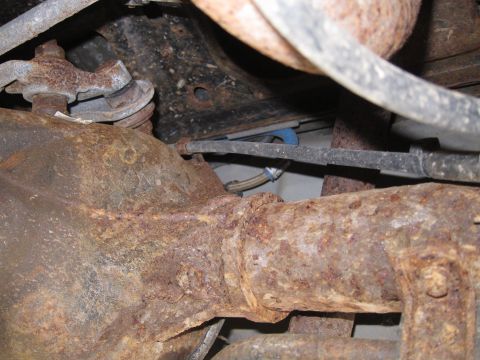 2001 Ford Crown Victoria - Close-up view of heavily rusted rear axle and suspension parts, showing significant corrosion.
